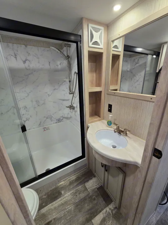 This modern RV rental bathroom features a shower, vanity, sink, and toilet, offering comfort and style.. Forest River Sandpiper 2023