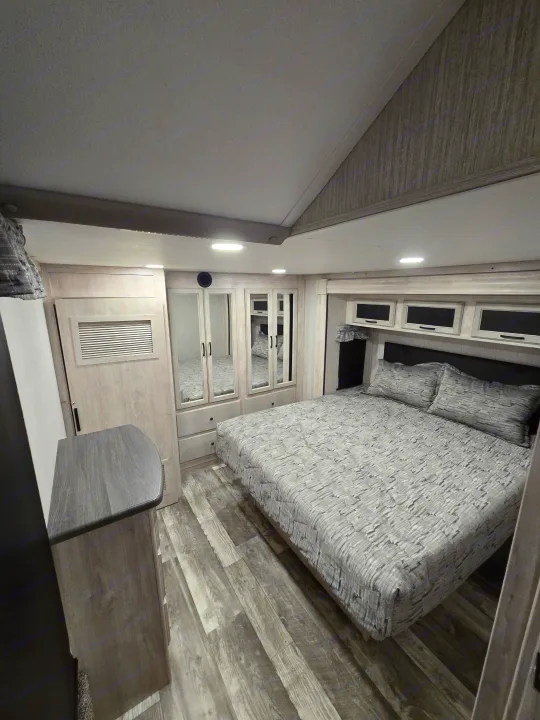Spacious, modern RV rental bedroom featuring a large bed, mirrored wardrobe, overhead cabinets, and wood-look flooring.. Forest River Sandpiper 2023