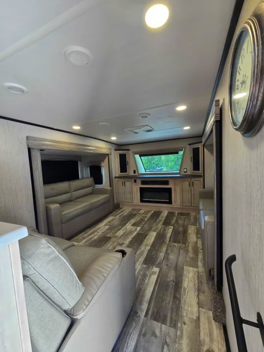 Modern RV rental living room with a cozy sofa, electric fireplace, wood-look floor, and ample natural light.. Forest River Sandpiper 2023