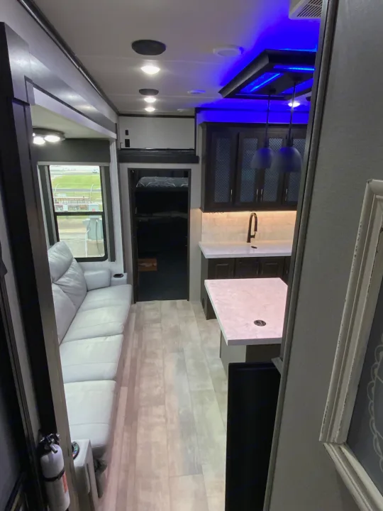 Spacious RV rental interior: light sofa, modern kitchen with blue lights, wood-look floor, and bunk area.. Grand Design Momentum 2024