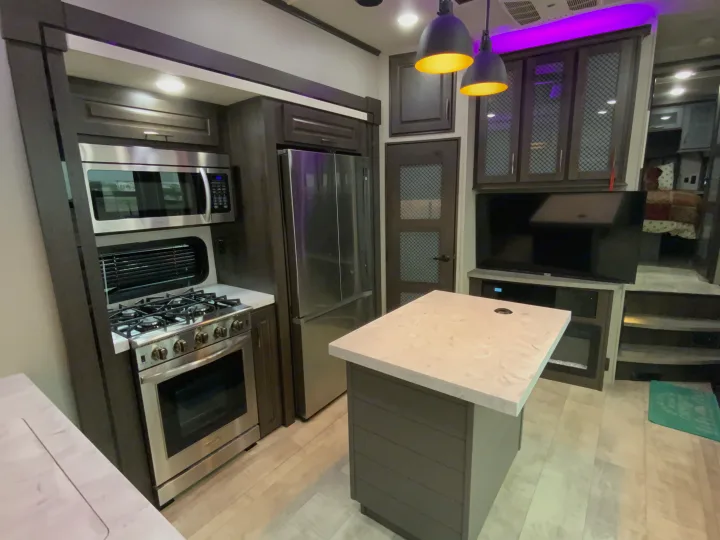 Spacious, modern RV rental kitchen & living area features stainless steel appliances, dark cabinets, and a central island.. Grand Design Momentum 2024