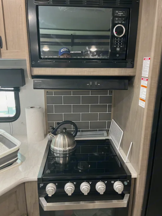 This rv rental kitchen showcases a Greystone microwave, stovetop, and oven. A kettle rests on the burner, ideal for compact cooking.. Keystone RV Hideout LHS 2020