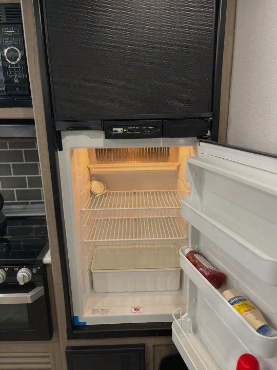 Inside an RV rental kitchen, featuring an open Norcold refrigerator with some condiments, microwave, and stove.. Keystone RV Hideout LHS 2020