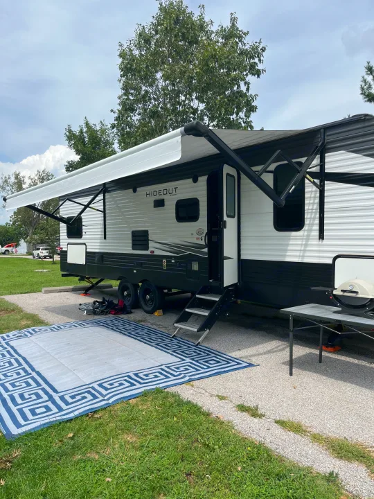 Full rv rental campsite setup: extended awning, outdoor rug, table, and grill ready for use.. Keystone RV Hideout LHS 2020