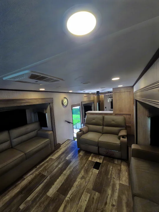 Inside a modern RV rental: a bright living area with plush gray sofas, wood-look flooring, and ceiling AC unit.. Forest River Sandpiper 2023