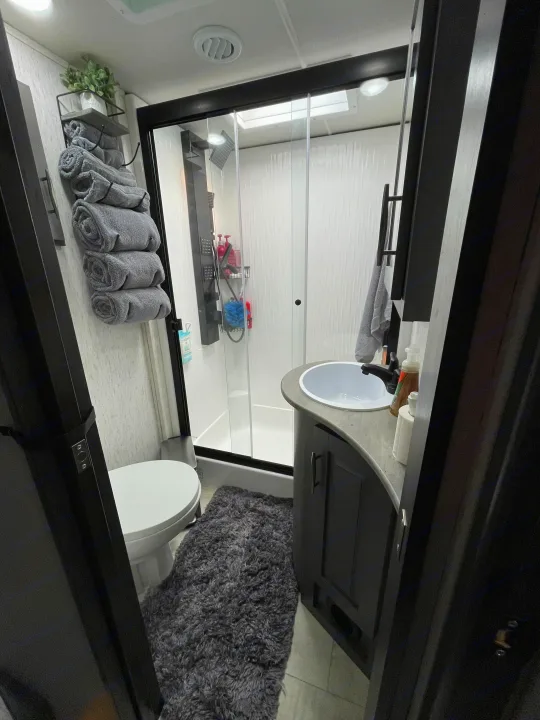 Compact and modern RV rental bathroom featuring a shower, toilet, and vanity with sink, complete with neatly rolled towels. Perfect for your travels.. Grand Design Momentum 2024
