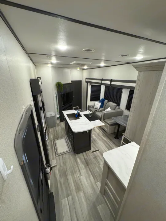 Bright RV rental interior showing a full kitchen, comfy living room, and dining table, all with wood-look floors.. Keystone RV Sprinter 2022