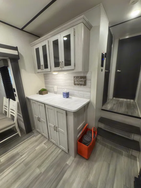 Modern rv rental kitchen/dining area with light wood finishes, white counters, and stairs to upper level.. Keystone RV Sprinter 2022