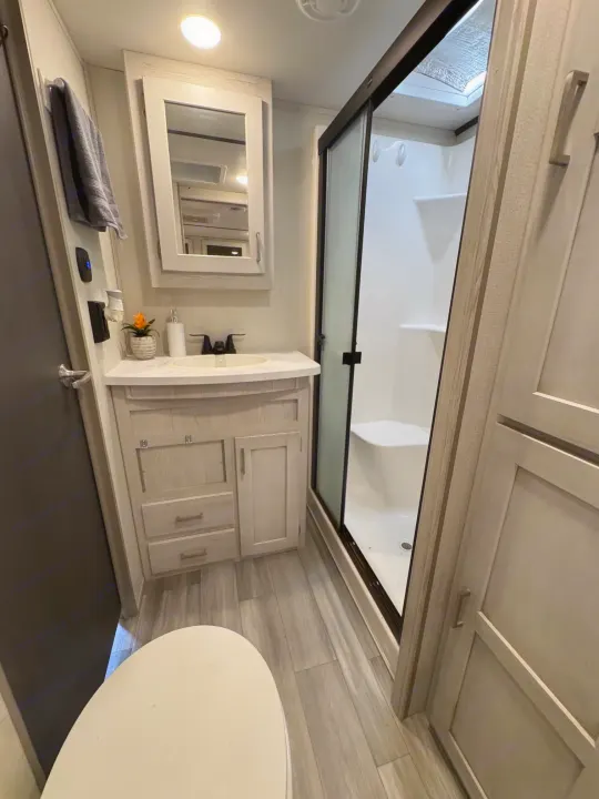 Bright RV rental bathroom with a modern glass shower, light wood-look vanity, mirror, and toilet. Ideal for your camper trip.. Keystone RV Sprinter 2022