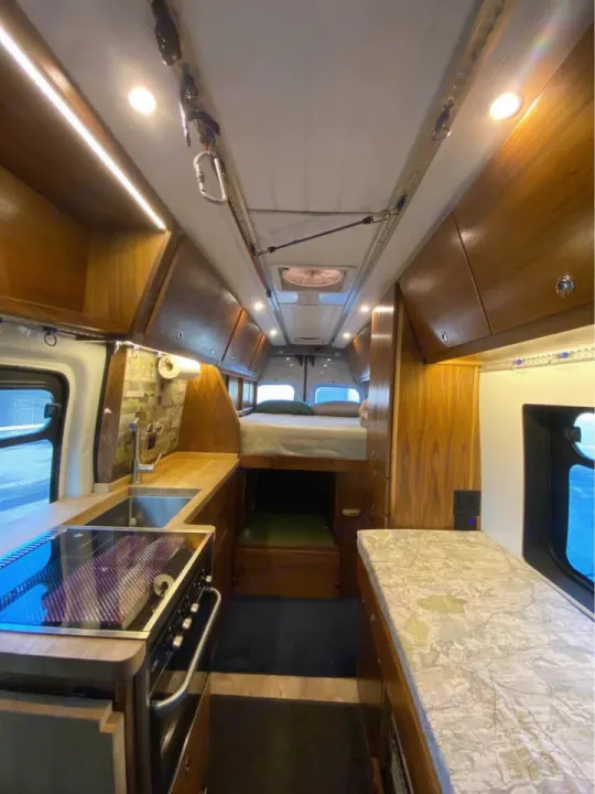 This cozy RV rental interior features a full kitchen, bed, and custom wood cabinetry, perfect for adventure.. Ford Transit 2018