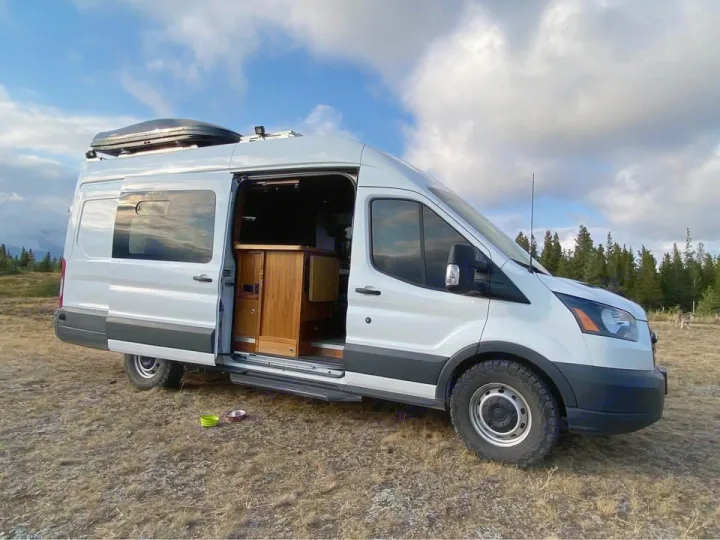 White camper van rv rental with open door, showing custom wood interior, parked off-grid.. Ford Transit 2018
