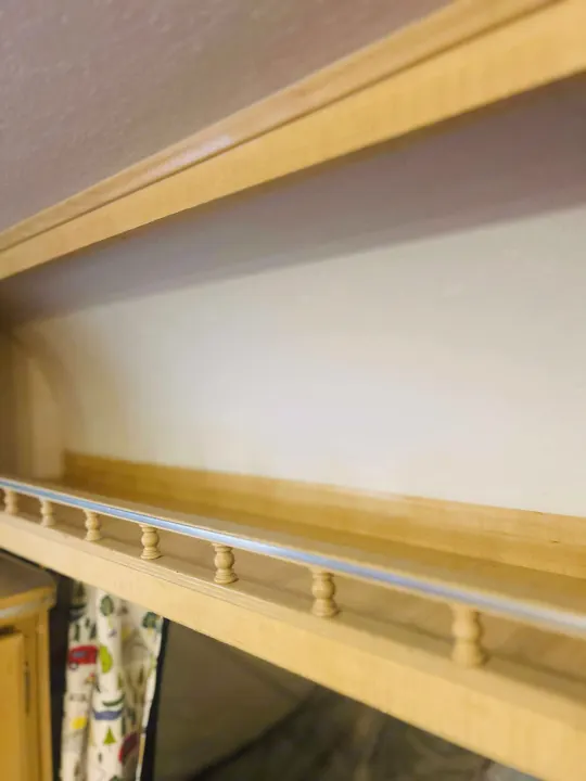 Light wood overhead shelf in an rv rental, featuring a safety bar with balusters for secure storage.. Forest River M-17 2005