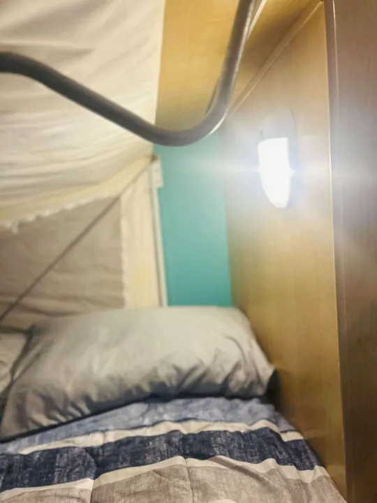 Comfortable sleeping area inside an RV rental, featuring a bed with striped comforter, pillow, and reading light.. Forest River M-17 2005