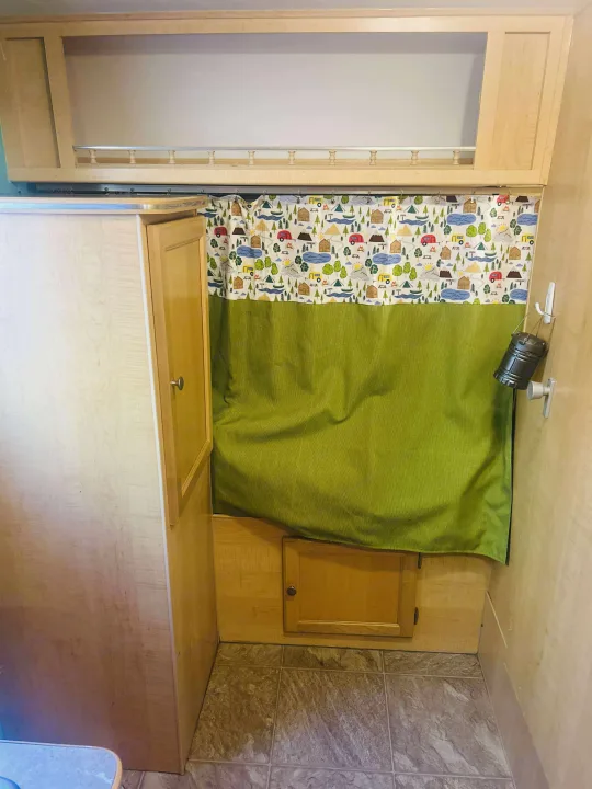 An RV rental interior with light wood cabinetry, an overhead shelf, a lively camping curtain, and a hanging lantern.. Forest River M-17 2005