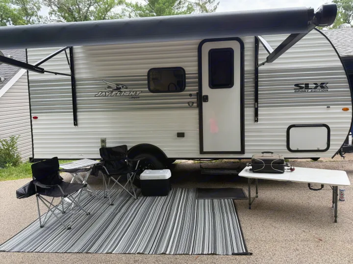 Jay Flight rv rental shows its outdoor living setup: awning, striped mat, chairs, cooler, and grill ready for use.. Jayco SLX Sport 2025