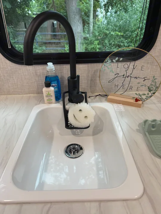 RV rental kitchen sink features a black faucet, dish soap, a happy scrub sponge, and a "LOVE grows HERE" sign.. Jayco SLX Sport 2025