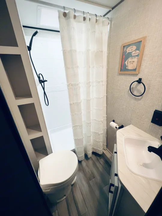 Clean RV rental bathroom with a white shower curtain, toilet, vanity sink, and quirky wall art.. Jayco Jay Flight 2024