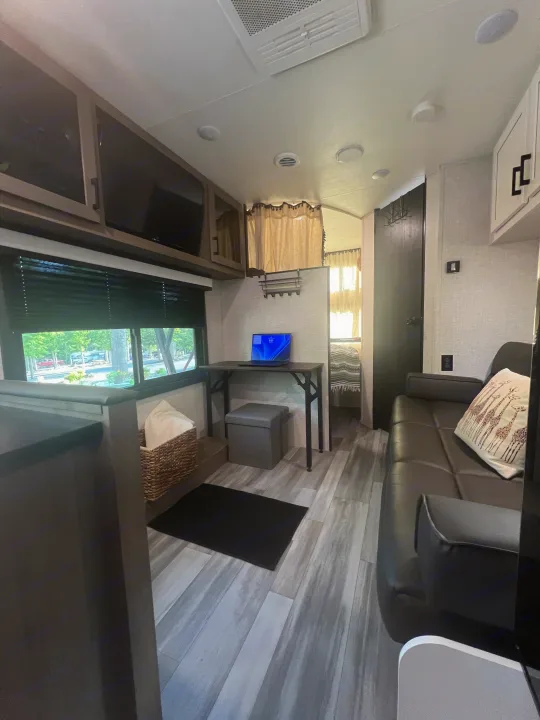 Spacious RV rental interior featuring a modern living area, work desk with laptop, and a window view of a campsite.. Jayco Jay Flight 2024