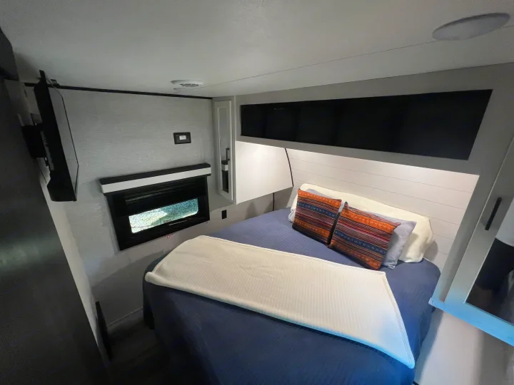 Experience comfort in this RV rental bedroom with a mounted TV, cozy bed, shiplap headboard, and compact window.. Jayco Jay Flight 2024