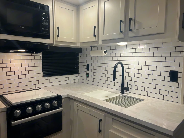 A modern RV rental kitchen featuring light cabinets, black appliances, subway tile backsplash, and a sleek sink area.. Jayco Jay Flight 2024