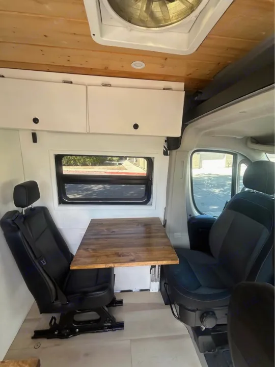RV rental interior: wooden ceiling, overhead storage, dining table, two seats, and a window. Ideal for campervan adventures.. Dodge Ram ProMaster 2021