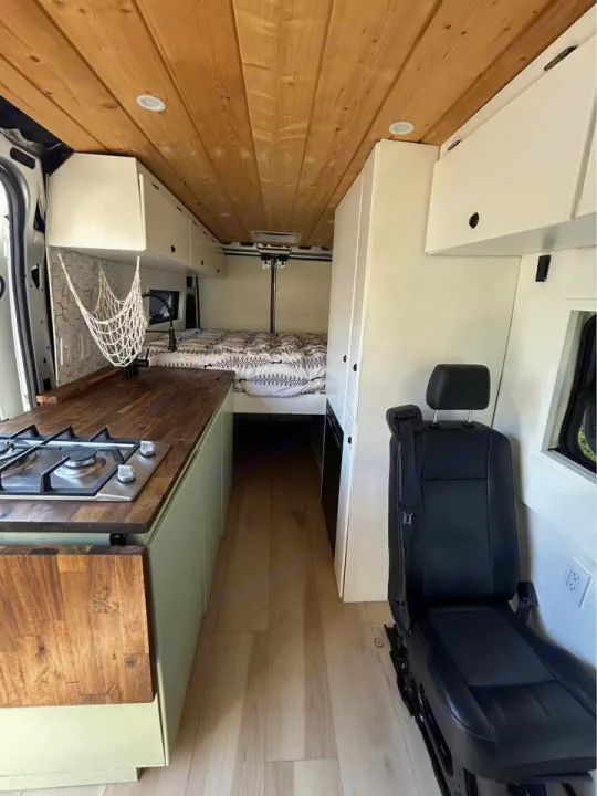 Discover this RV rental's cozy camper van interior: a compact space featuring a bed, kitchenette with stove, and wood ceiling.. Dodge Ram ProMaster 2021