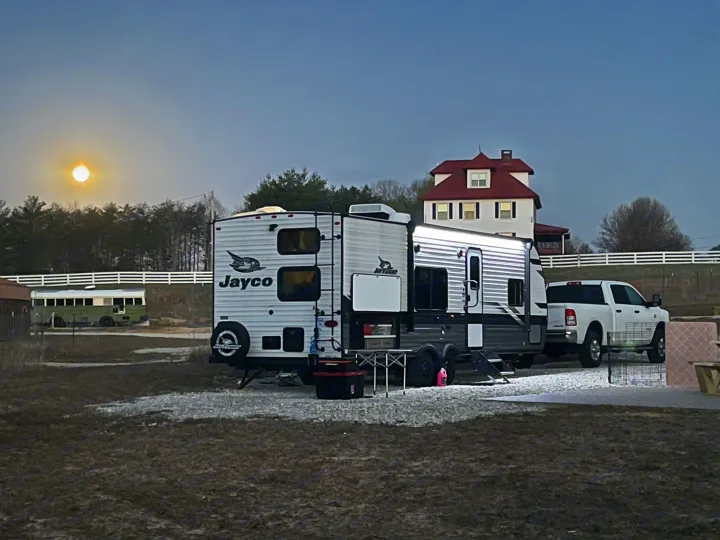 An RV rental with a pickup truck under a bright moon at twilight, near a house and green bus.. Jayco Jay Flight 2024
