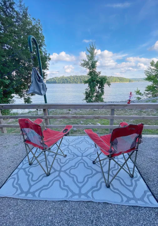 Enjoying a peaceful lakeside retreat from our RV rental. Two red chairs await on a mat, facing the beautiful water and distant hills.. Jayco Jay Flight 2024