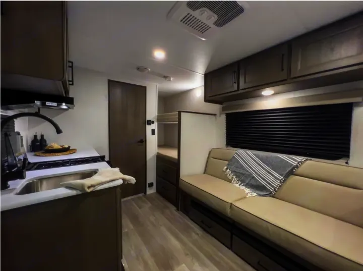 Bright rv rental interior features a kitchen, sofa, bunks, light wood floors, and an overhead AC unit.. Grand Design Transcend One 151BH 2025