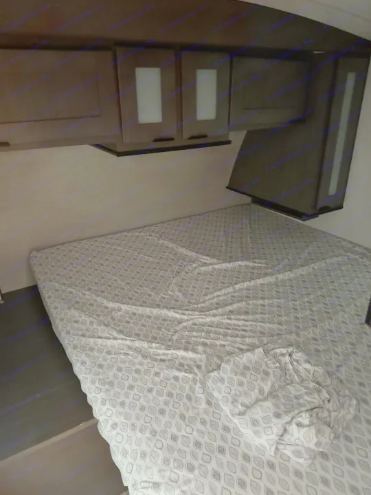 Dimly lit RV rental bedroom featuring a bed with patterned sheets and dark wood overhead cabinets.. Other Other 2021