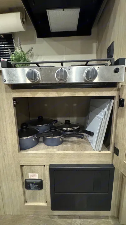 Compact RV rental kitchen with a GE Profile stove, cookware storage, and safety features like a CO detector.. Coachmen Catalina 2025