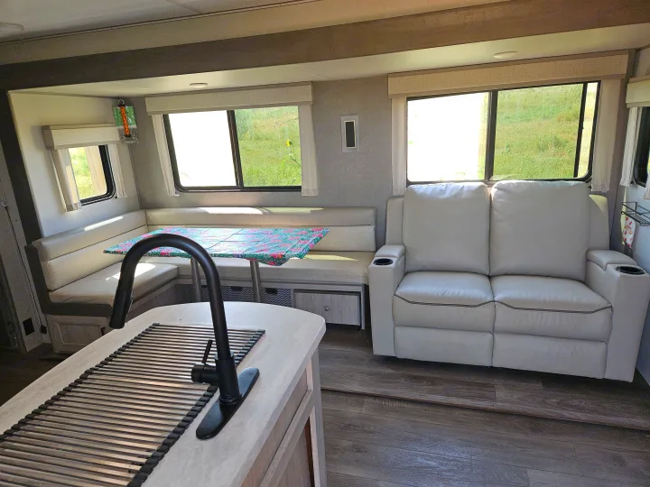 Bright RV rental interior with dinette, recliner sofa, kitchen island, and scenic window views.. Coachmen Catalina Legacy 2024