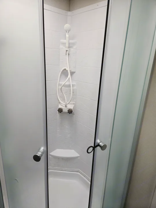 This RV rental features a compact, white shower with a handheld showerhead and frosted doors.. Coachmen Catalina Legacy 2024