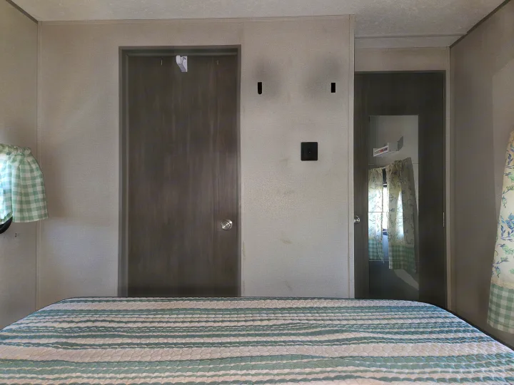 Compact RV rental bedroom featuring a striped bed, two doors, and patterned curtains. Cozy travel space.. Coachmen Catalina Legacy 2024