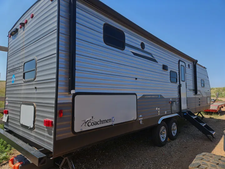 A large, modern Coachmen travel trailer, parked outdoors on gravel. Consider this RV rental for your next trip!. Coachmen Catalina Legacy 2024