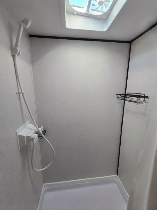 RV rental's clean, compact shower: handheld showerhead, storage caddy, and bright skylight.. Colman 23B 2025