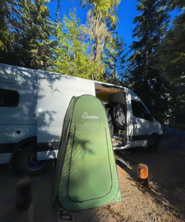 White RV rental van at a forest campsite with a green Wolfwise privacy tent for outdoor showers.. Mercedes Sprinter 2012