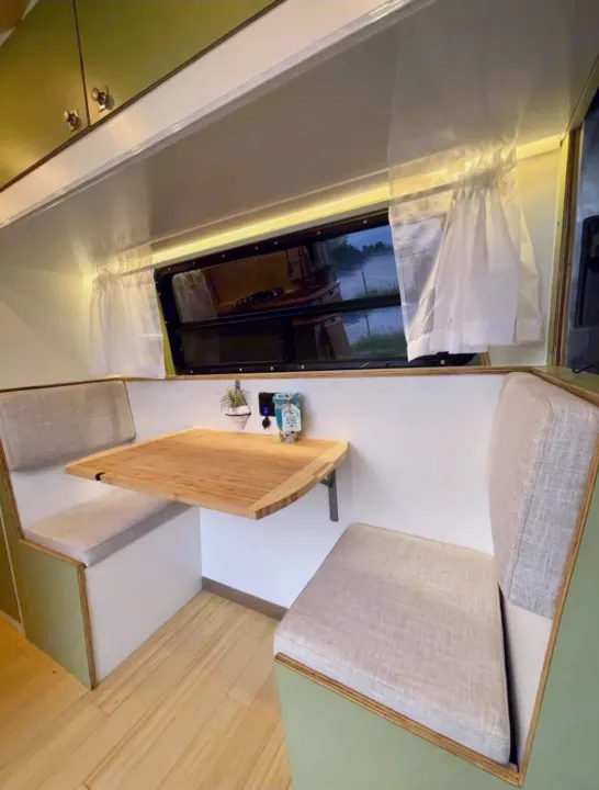 This RV rental interior features a compact dinette with light green benches, a folding wood table, and a scenic window view.. Mercedes Sprinter 2012