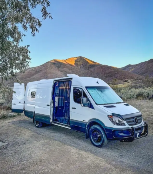 White Sprinter rv rental camper van, doors open, parked in a scenic mountain landscape, perfect for adventure.. Mercedes Sprinter 2012