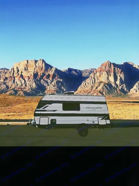 An RV rental, a white and black travel trailer, is parked on a dark surface, set against majestic red rock mountains under a clear blue sky in a desert landscape.. Grand Design Transcend One 151BH 2025