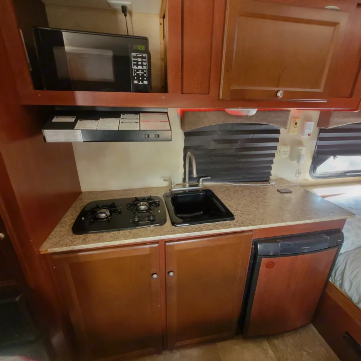 RV rental kitchenette features microwave, gas stove, sink, and compact fridge, ideal for travel.. Coachmen 16fb 2019