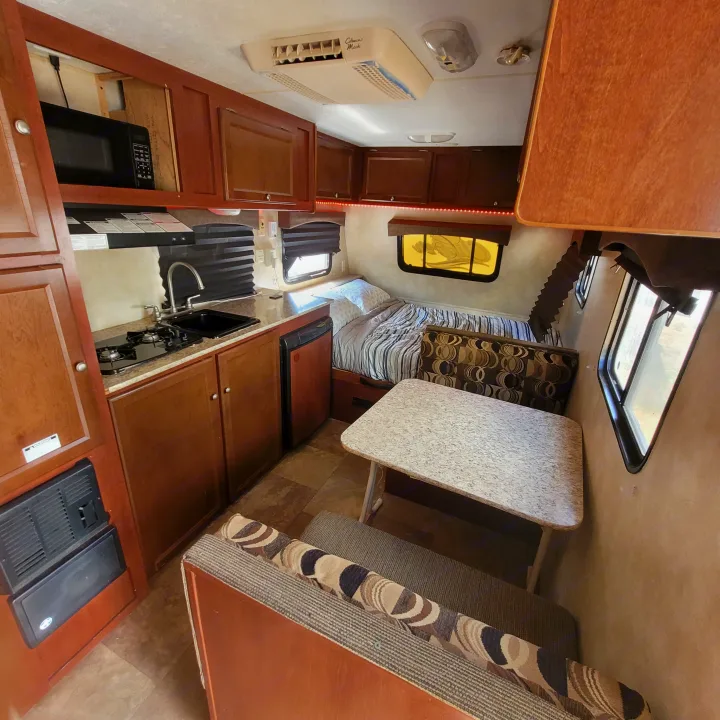 RV rental interior: modern kitchen, dinette with seating, and a bed. Ceiling AC & wood cabinetry visible.. Coachmen 16fb 2019