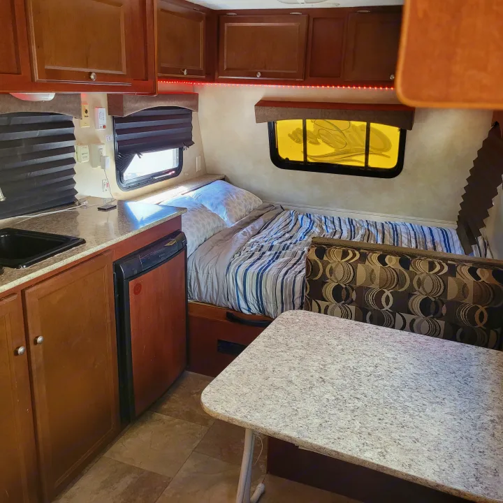 RV rental interior: kitchen sink, counter, cabinets, bed, and dinette with patterned cushions. Red LED lights.. Coachmen 16fb 2019