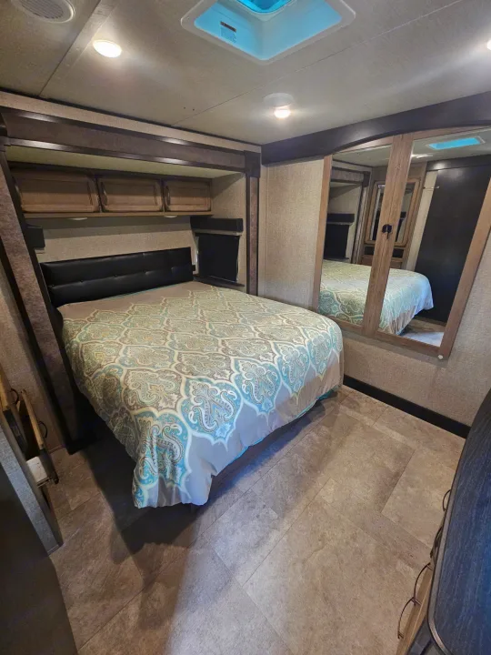 Comfortable RV rental bedroom with patterned comforter, overhead storage, and mirrored wardrobe. Perfect for travel.. Grand Design Transcend 2020