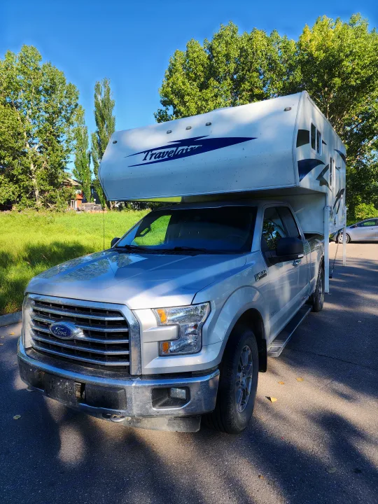 Silver Ford F-150 with a Travelaire truck camper, perfect for an RV rental. Ready for adventure, parked among trees.. Ford Ford F150 2017