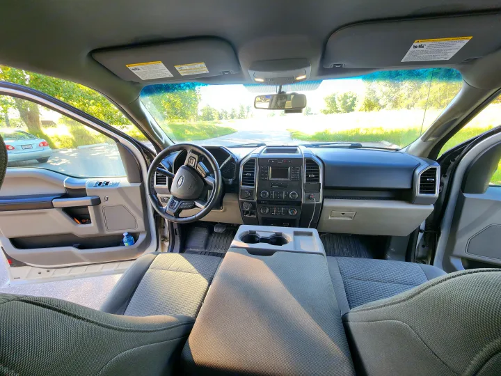 Spacious truck interior, ideal for an RV rental trip, with open doors to a scenic road. View of dash, steering wheel, seats.. Ford Ford F150 2017