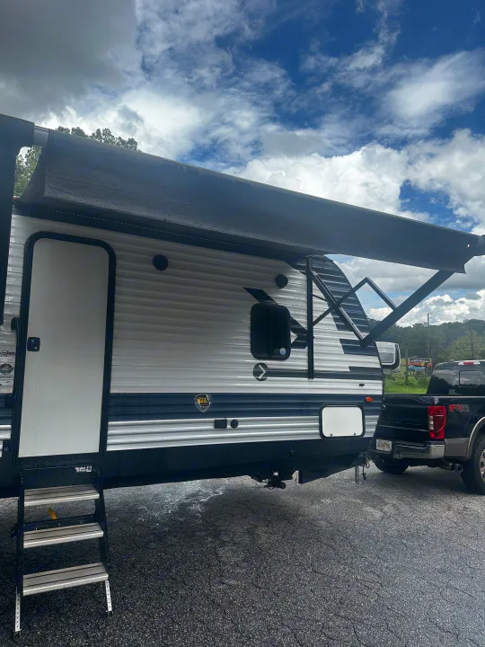 This white and blue RV rental, a travel trailer with an extended awning and Solid Step, is hitched to a black pickup.. Crossroads RV Zinger 2020