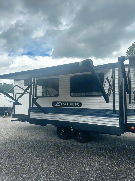 A Zinger RV rental travel trailer with an extended black awning, parked on gravel under a cloudy sky.. Crossroads RV Zinger 2020