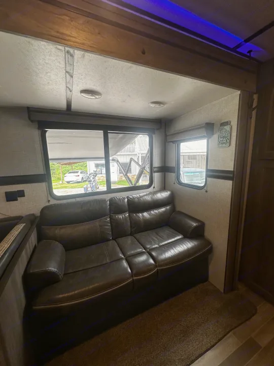 Cozy rv rental interior showcasing a brown leather sofa, large windows with outside views, and overhead blue LED lighting.. Crossroads RV Zinger 2020