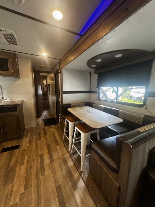 Spacious RV rental interior featuring a cozy dining area with table and booth seating, plus a peek into the kitchen and hallway.. Crossroads RV Zinger 2020